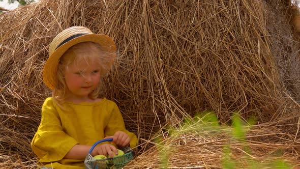 A Little Blond Girl in a Straw Hat is Giving a Green Apple to Her Sister