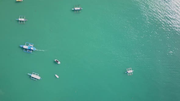 Aerial view directly down on emerald green waters with traditional filipino boats tracking shot to E