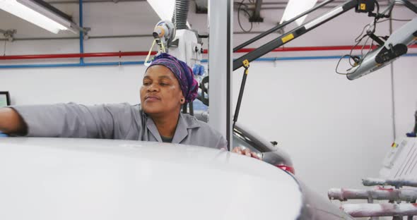 African American female car mechanic cleaning the roof of a car with a rag