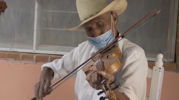 Closeup shot of a Hispanic aged musician with a hat and a mask playing violin on the street