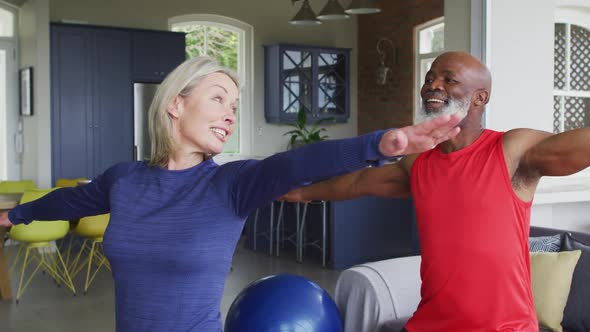 Mixed race senior couple performing stretching exercise together at home