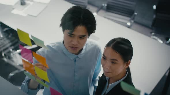 Asian Colleagues Looking At Notes On Visualization Board In Office