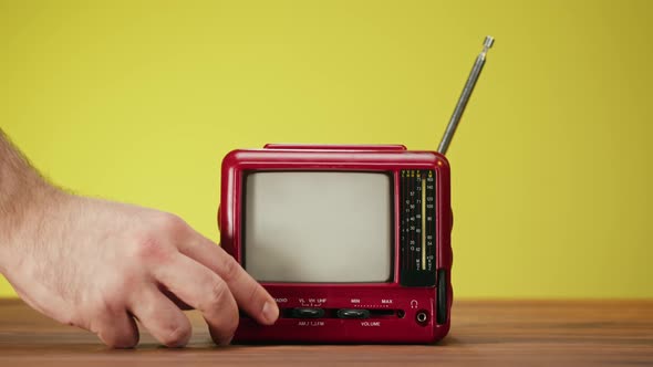 Turning on Small Old Television with Grey Interference Screen on Yellow Background