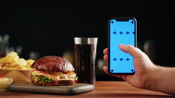 Tasty Burger and Smartphone with Blue Chroma Key Screen Closeup Cooked Juicy Sandwich Fast Food