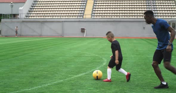 Black Coach Teaching Boy to Handle Ball on Football Pitch