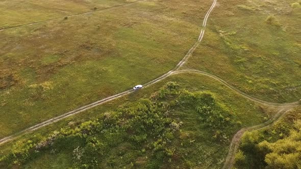 White Car on Scenic Unpaved Road with Fork Aerial Tracking Shot on Sunset