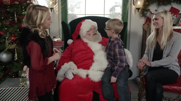 Boy jumping up on Santa's lap as mom sits and smiles