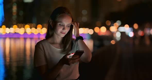 Young Girl in the Night City Writes Text Messages in a Smartphone