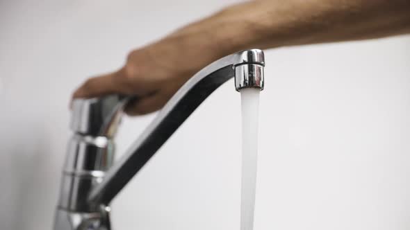 Male hand turns on silver faucet and fills water glass, close-up