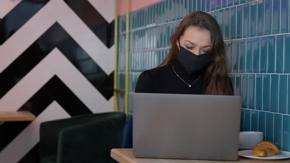 Attractive Longhaired Girl in Black Protective Mask Messaging in Cafe