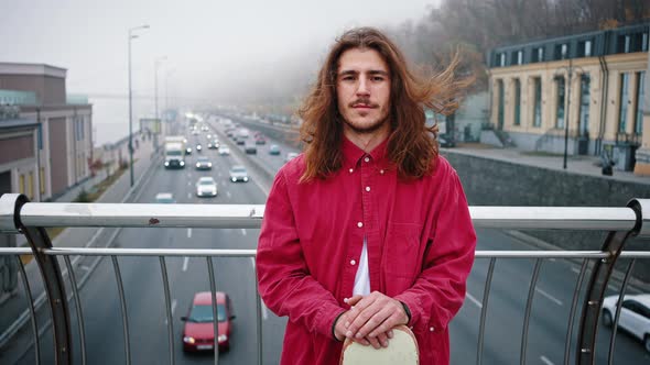 Guy with a Longboard in His Hands is Standing on the Bridge