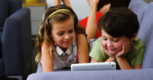 Siblings using digital tablet in living room