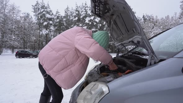 Woman Shines Phones Under the Hood of a Broken Car in Winter