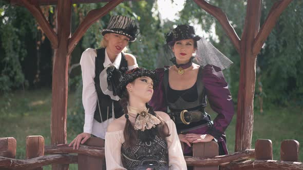 Relaxed Caucasian Young Woman Sitting in Pavilion with Adult Friends Standing Behind Looking at