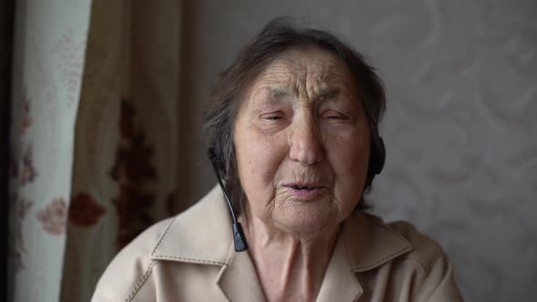 Very Old Woman in Headphones Making Video Conversation in Their Home