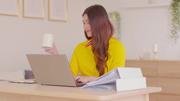 Beautiful creative asian young woman using laptop computer and holding coffee cup working