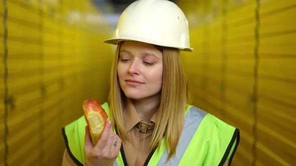 Young Woman Smelling Fast Food Bun Standing in Warehouse Shaking Head No Gesture Looking at Camera