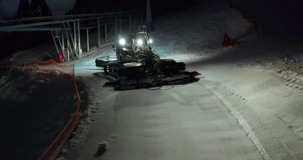 Aerial View. Snow Grooming Snowcat Machines Fix Trail on Ski Resort Slope at Night.