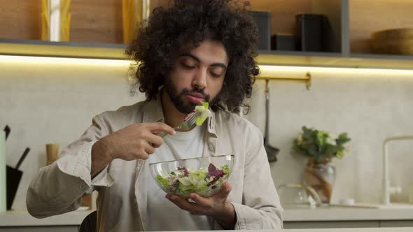 Egyptian Man Enjoys Eating Salad at Table in Modern Kitchen