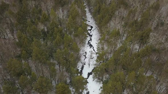 Aerial shot of snowy river from above slowly tilting up to reveal forest and mountains