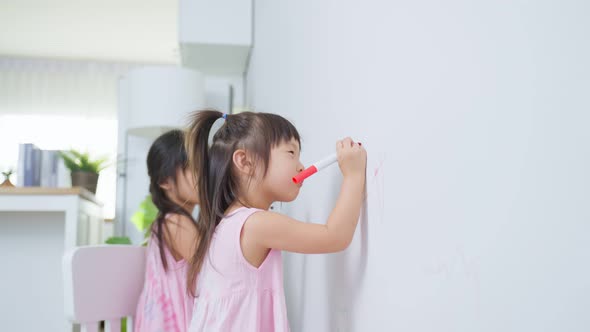 Asian young sibling kid girl enjoy enjoy creativity activity paint on white wall in living room.