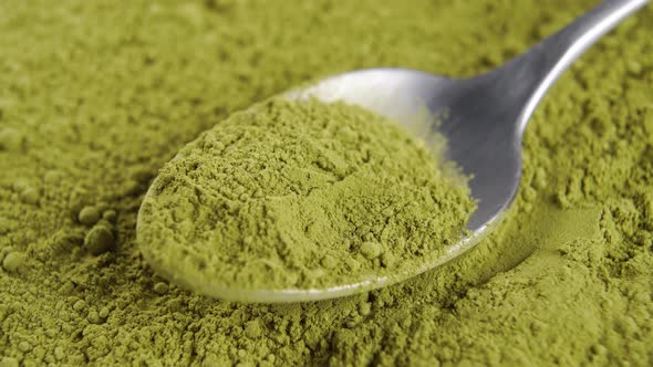 Teaspoon with powdered matcha green tea in heap of powder. Macro