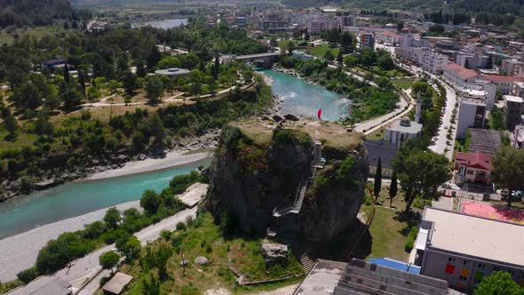 Birds eye view of Permet township around Vjosa river and surrounded by mountains and greenery.