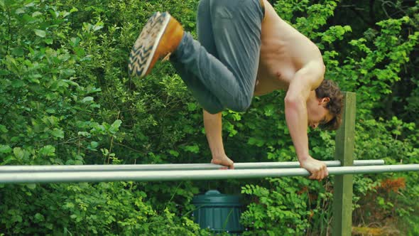 Young fit topless man L-sit to handstand press on parallel bars outdoors home gym