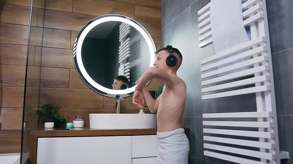 Satisfied Teen Boy with Towel on His Body Cleaning Teeth and Listening Music in Headphones