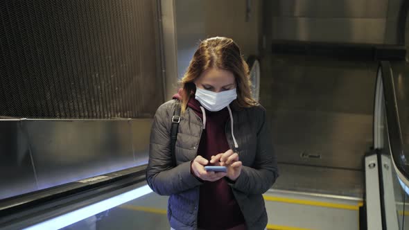 Student on Escalator Wearing Facial Mask Uses Mobile Phone in the Metro Station