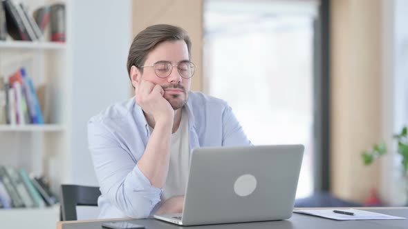 Man in Glasses with Laptop Thinking in Office