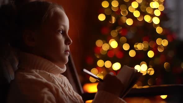 Closeup Face of Cute Little Girl Writing Christmas Letter to Santa Claus on Background Xmas Tree