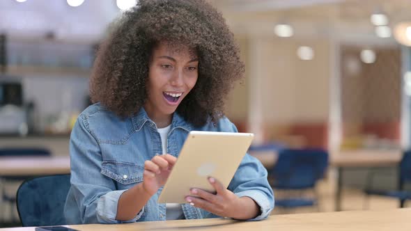 African Woman Celebrating Success on Tablet at Work