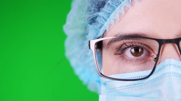 Green Background. Close-up, Eye, Part of Female Doctor Face in Glasses, in Blue Medical Mask