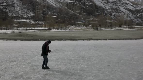 Aerial Circle Dolly Around Adult Male Walking Across Frozen Khalti Lake. Slow Motion