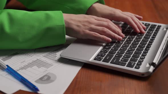 Manager Types Report on Laptop Sitting at Wooden Table