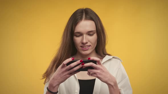 Young Adult Caucasian Woman Winning Online Video Game on Her Smartphone Bright Yellow Background