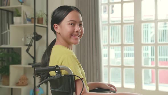 Asian Kid Girl Sitting In A Wheelchair Smiling And Looking At Camera Near Door