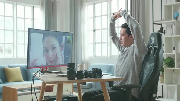 Asian Cameraman Stretching And Leaning Back While Using Desktop Computer For Editing Photo At Home