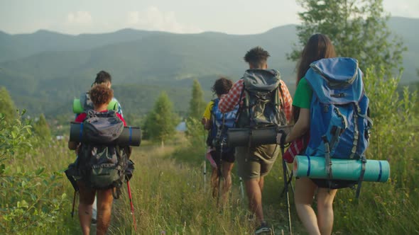 Diverse Multiethnic Backpackers with Hiking Poles Descending Down Mountain Trail at Sunset