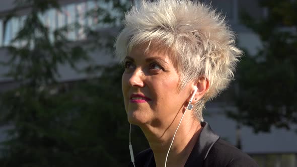 A Middle-aged Businesswoman Listens To Music on a Smartphone in an Urban Area - Closeup