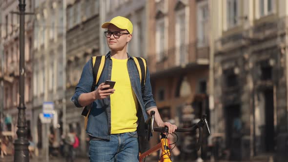 A Young Happy Delivery Man is Going and Texting on a Smartphone