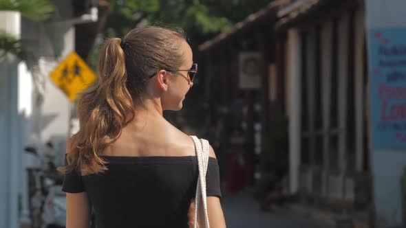 Woman Enjoys Promenade Past Buildings Against Bright Sun