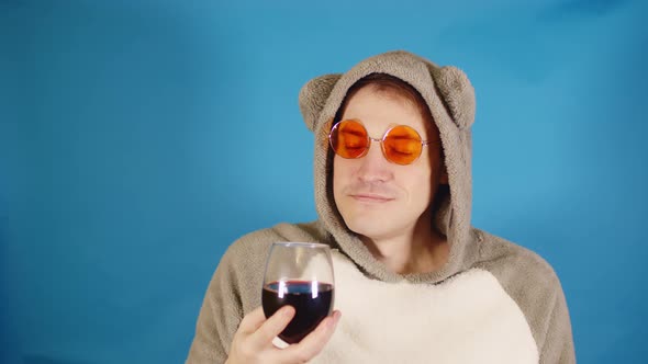 Man in Sunglasses and Hoodie with Ears Sniffs Aroma of Red Wine on Blue Background
