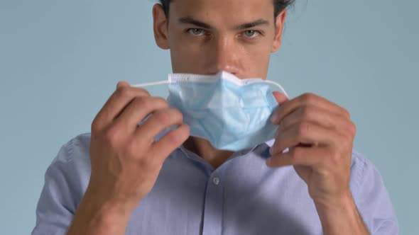 A Handsome Man Demonstrating The Proper Wearing Of Surgical Face Mask Standing Against Light Blue Ba