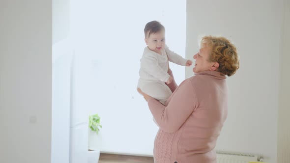 Elderly Woman Holding Her Baby Granddaughter Kiss at Home Young and Old People Together