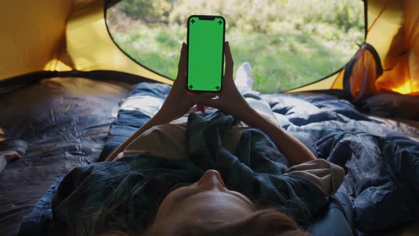 Handheld Firstperson View Female Holding a Smartphone with a Green Screen While Lying in a Tent