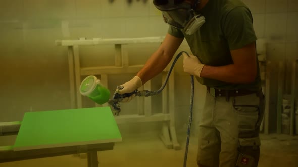 Painter Coloring a Piece of Wood with Green Color and Electric Spray Paint Machine