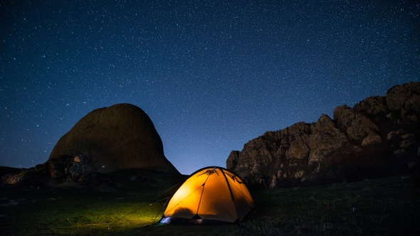 Time-lapse. Glowing camping tent in the mountains under a starry sky