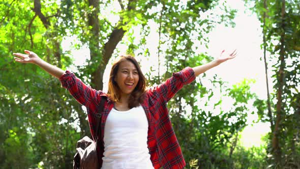 Happy young Asian woman traveler with backpack walking in forest.